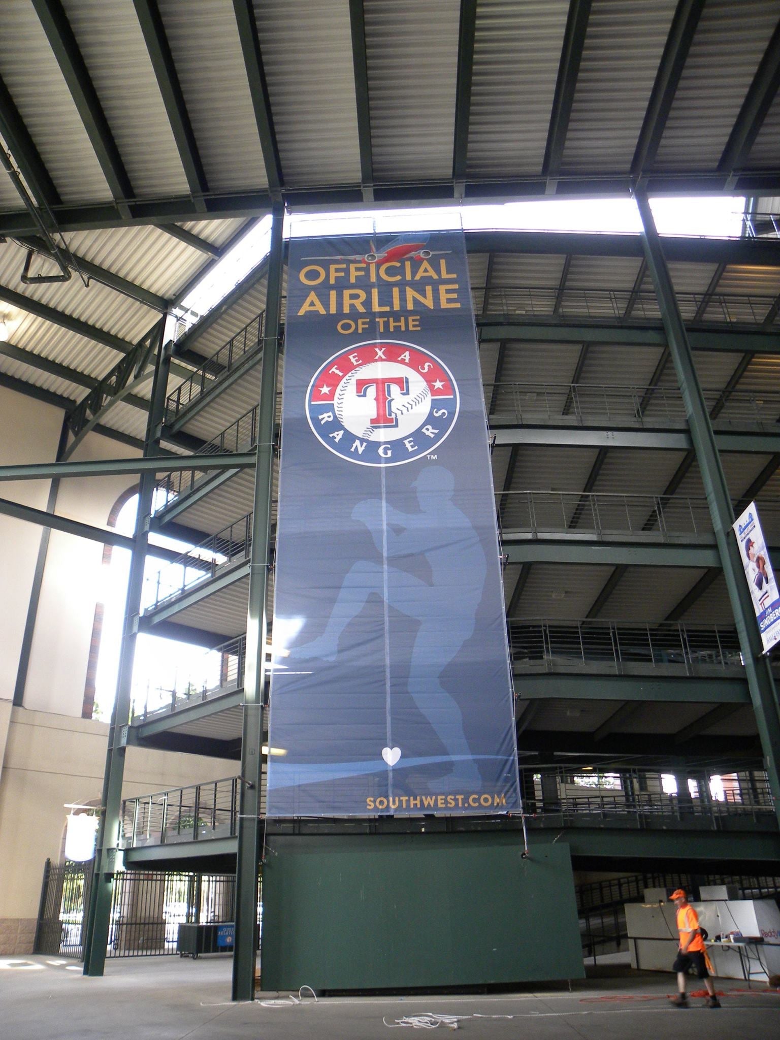 A close-up view of a large vertical mesh banner inside Globe Life Field in Arlington, Texas. The banner features the Texas Rangers logo with text indicating Southwest Airlines as the "Official Airline of the Texas Rangers."