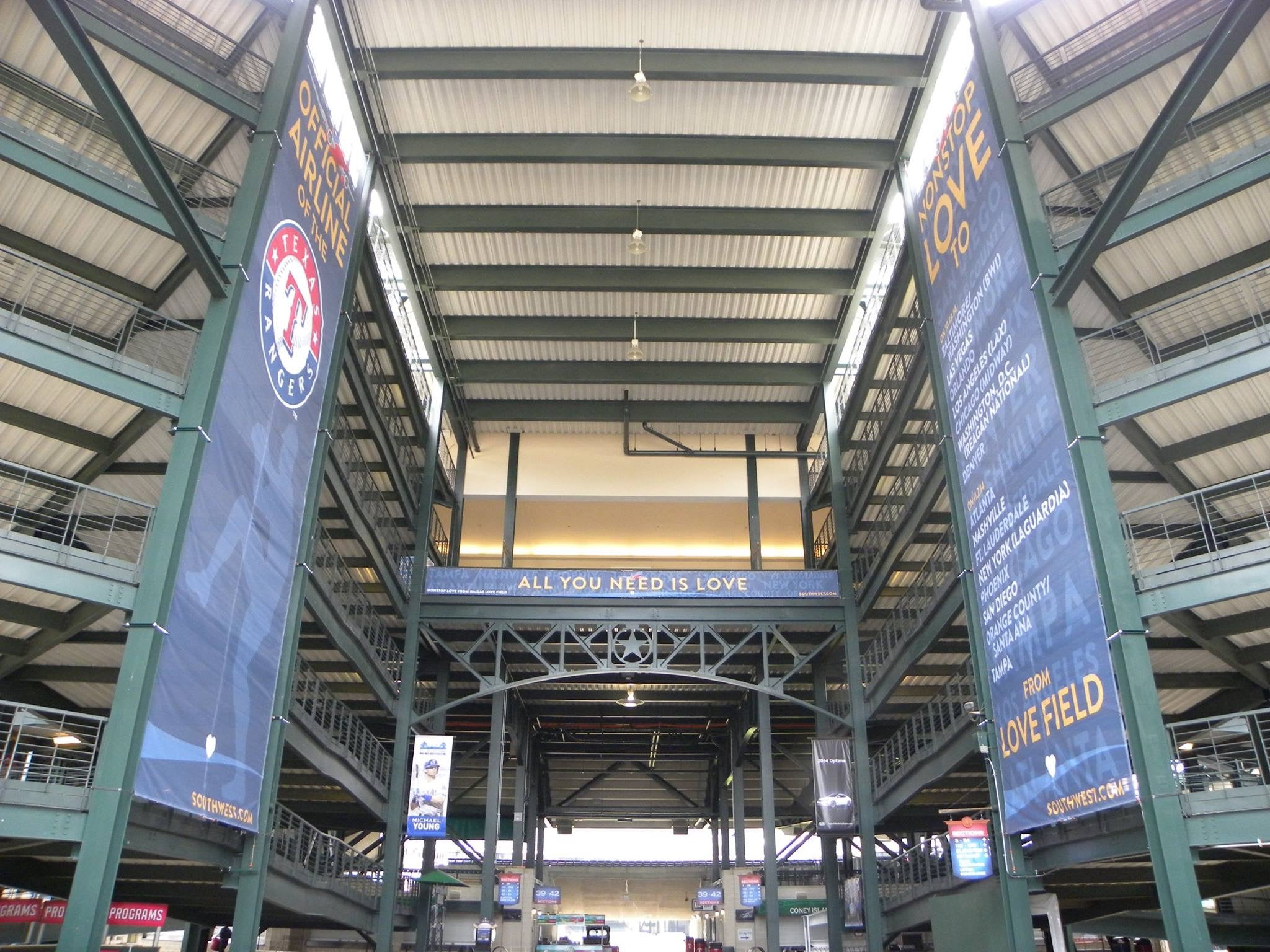 A set of three large mesh banners displayed inside Globe Life Field in Arlington, Texas. The banners showcase branding for the Texas Rangers and Southwest Airlines, with the slogan "All You Need is Love" in the middle.