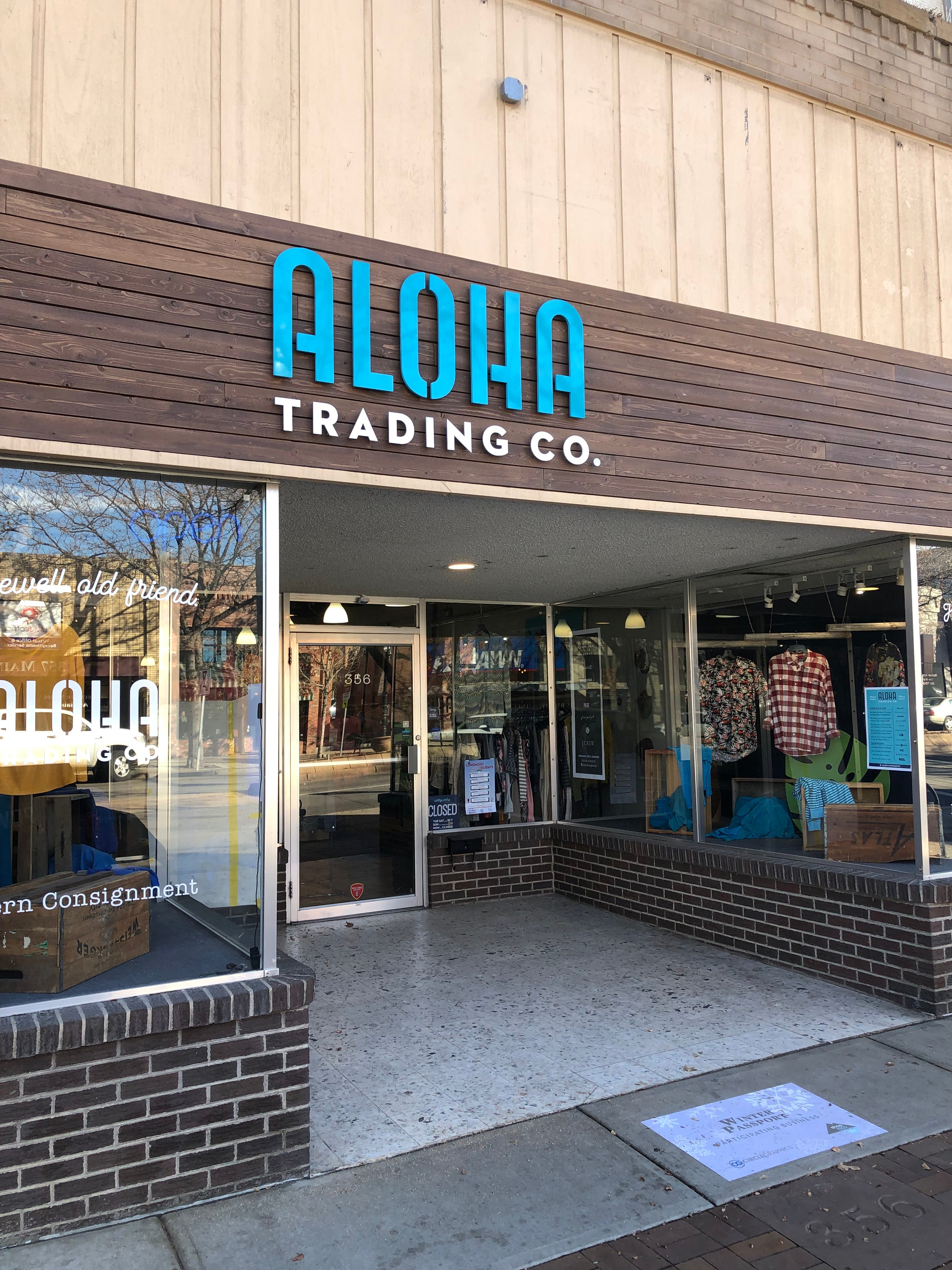 A bright blue, custom-fabricated outdoor sign for Aloha Trading Co., located in Boulder, Colorado. The store's name is mounted on a wooden facade, standing out against the natural wood texture, giving the storefront a modern and inviting look.