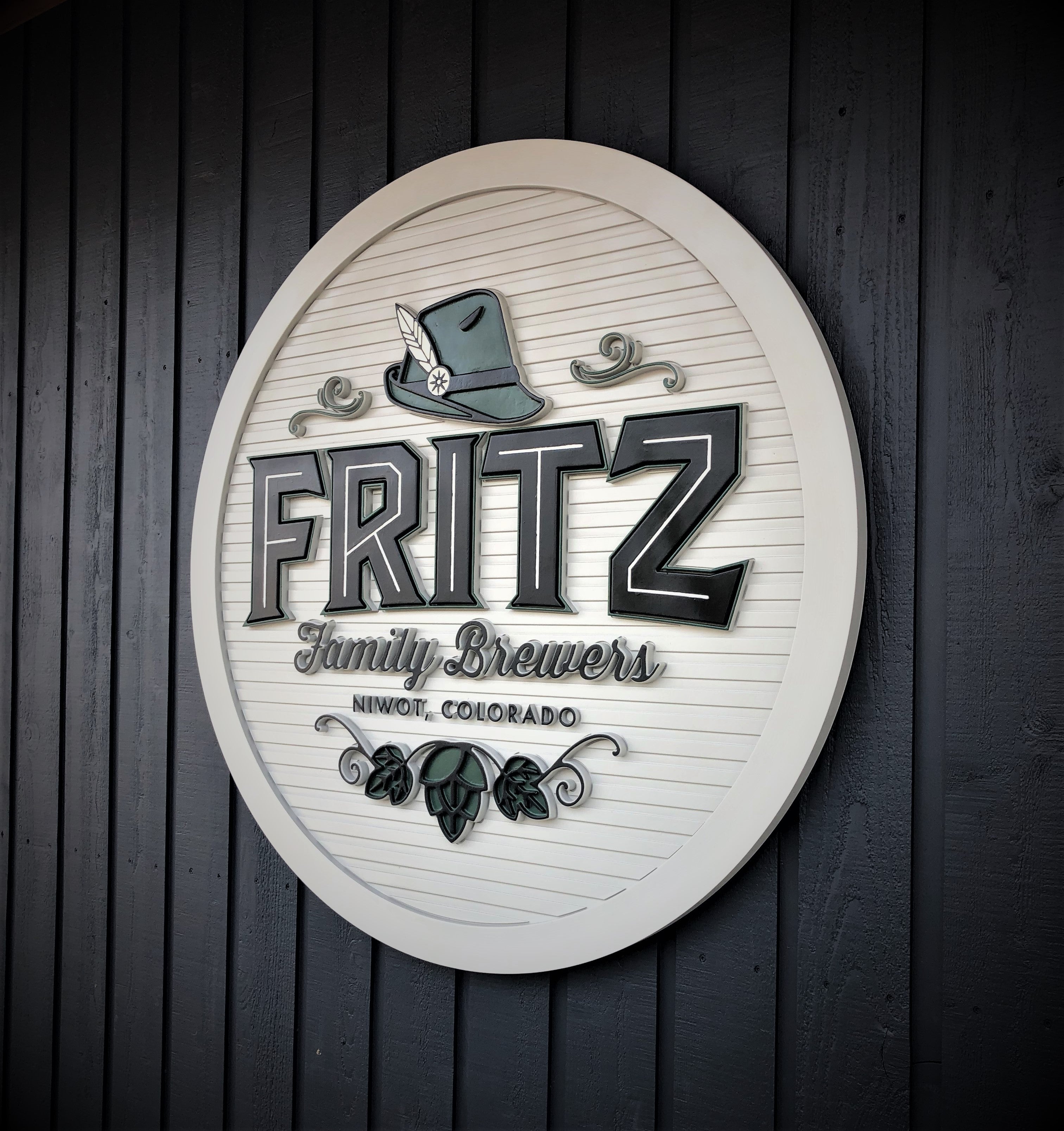 A lobby wall-mounted sign for Fritz Family Brewers in Niwot, Colorado. The circular sign features raised lettering with the brewery’s name and a decorative hat and hop design, delivering a polished and professional look.