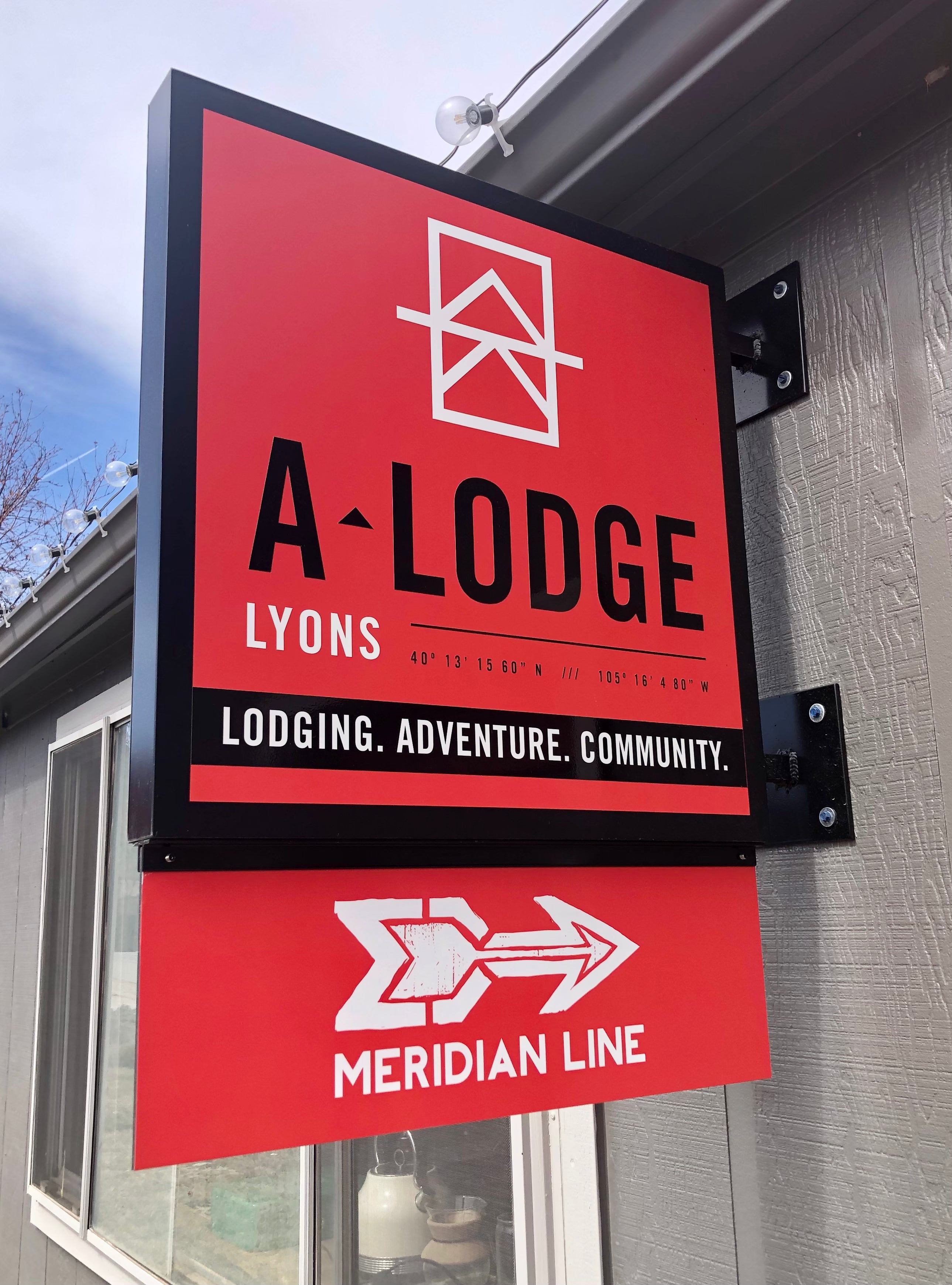 A wall mounted panel sign for A-Lodge in Lyons, Colorado. Showcasing their vibrant red colored background and logo, drawing attention from the streetside.