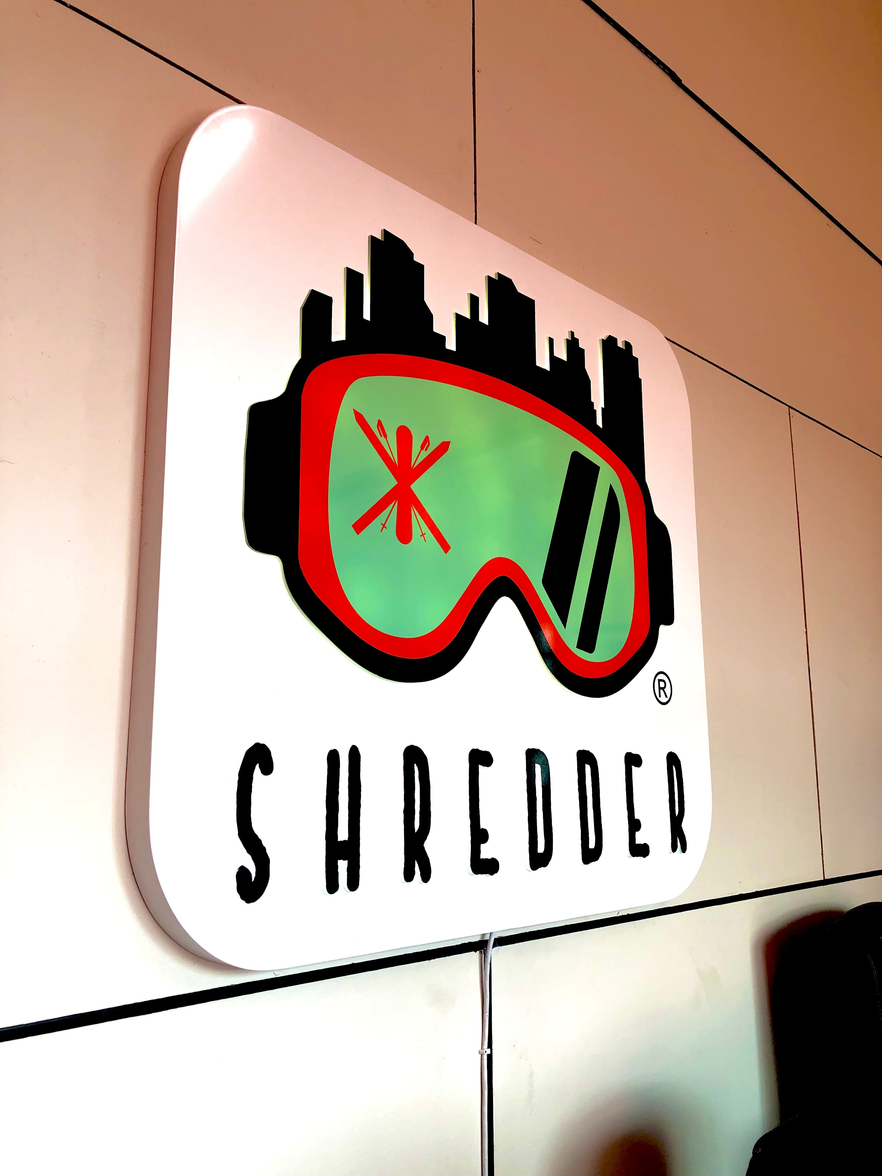 A lobby sign for Shredder: Indoor Ski and Snowboard School in Lafayette, Colorado. Featuring their unique and stylish logo with attractive colors on a white background.