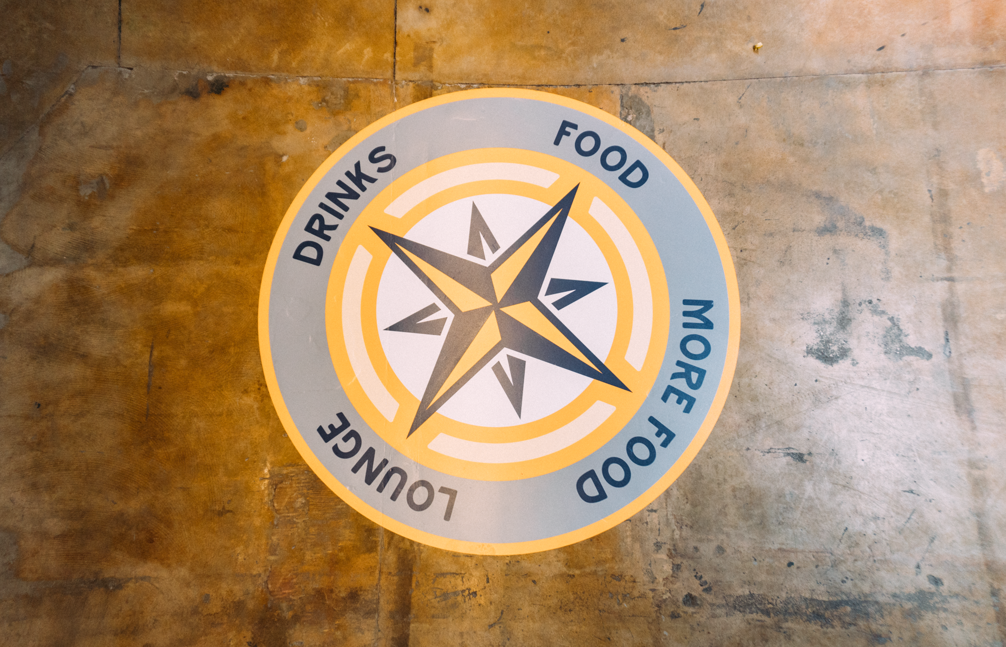 An interior floor wrap at Parkway Food Hall in Longmont, Colorado, featuring a colorful design with a large compass motif at the center, surrounded by decorative elements that enhance the dining atmosphere.