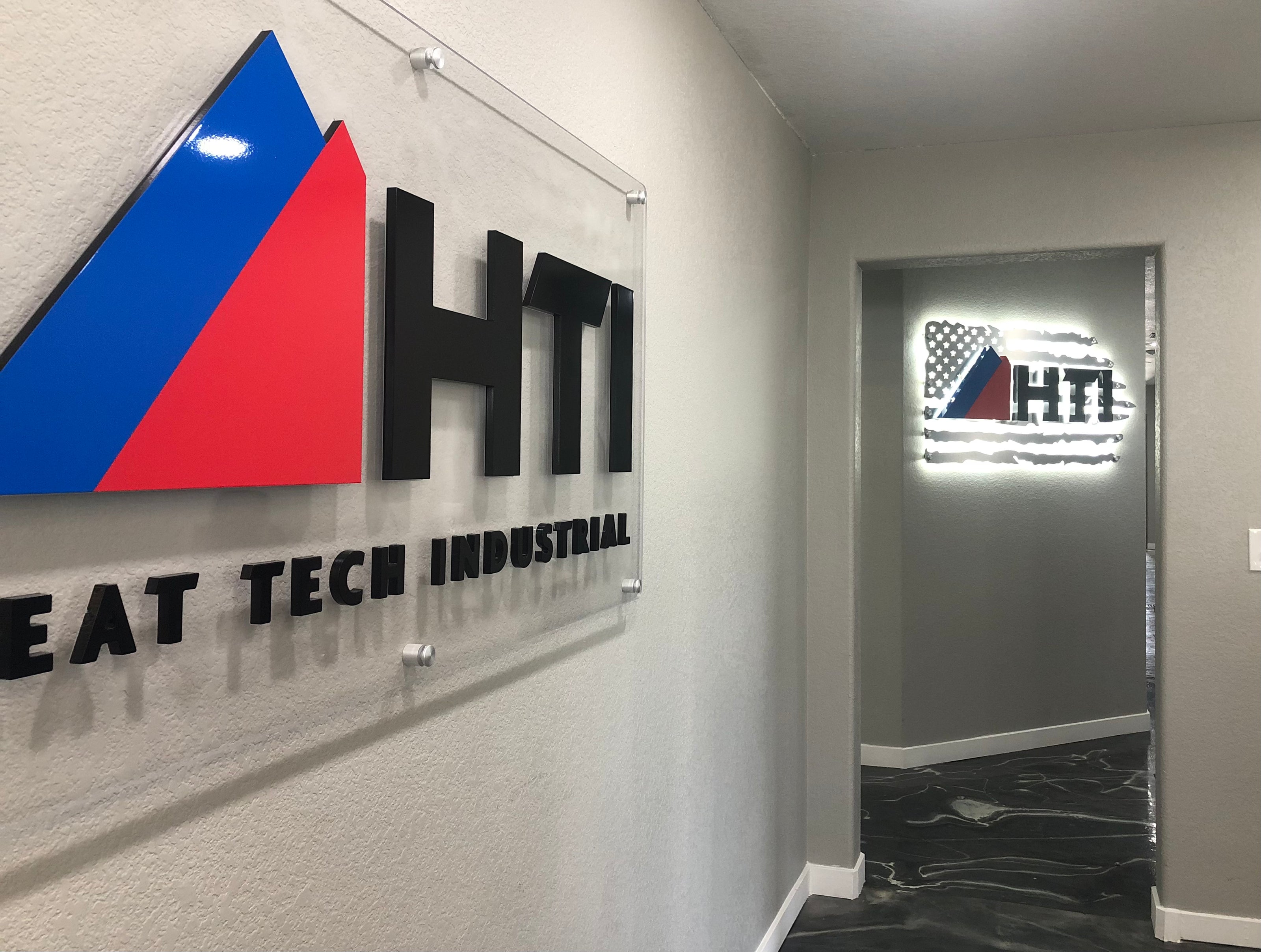 HTI Heat Tech Industrial's pair of indoor signs at their Frederick, Colorado location. One being an acrylic sign atop a clear background, the other an illuminated acrylic sign with the American flag as its background.