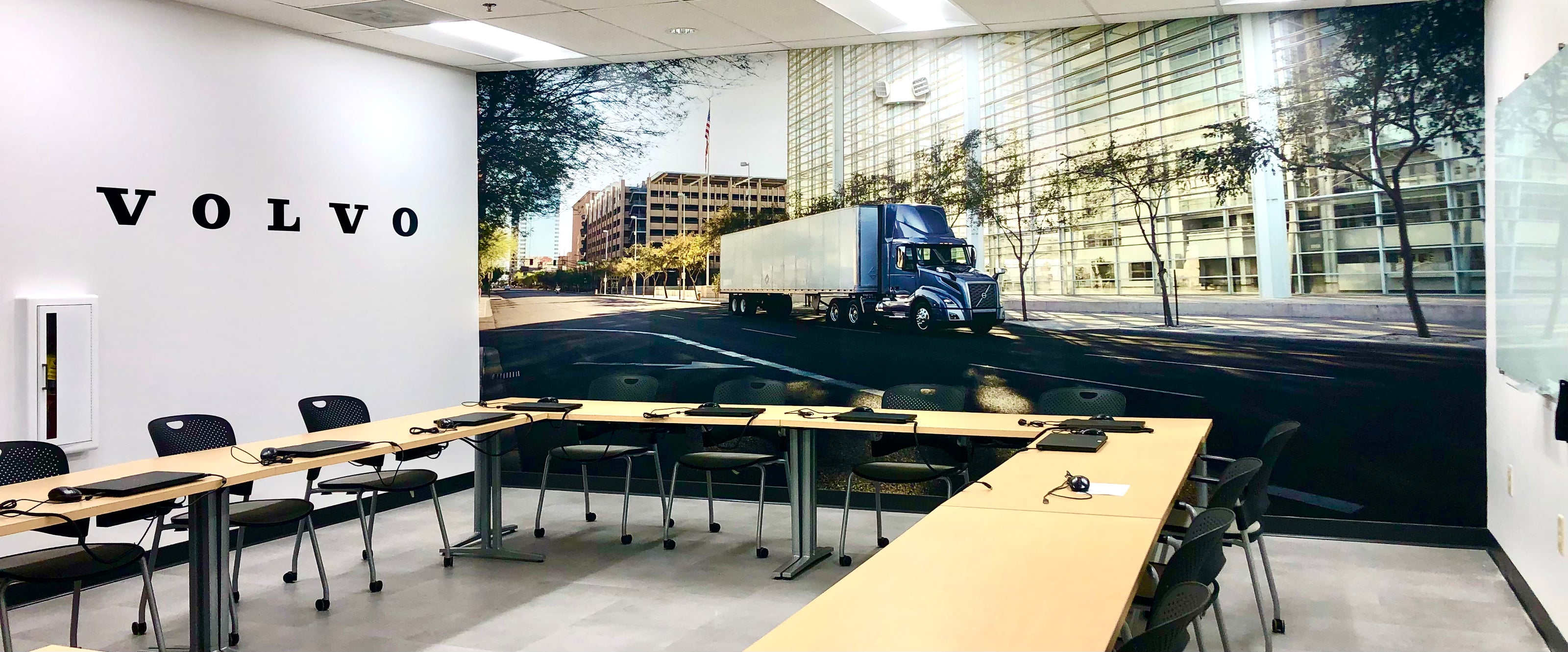 A large vinyl wall wrap and vinyl lettering for Volvo inside of their Atlanta, Georgie conference room. Featuring a Volvo truck driving through the streets of Georgia on a sunny day, complimented by their name in vinyl lettering to the side.