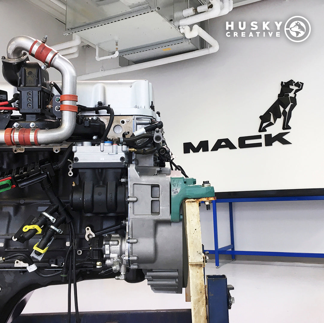 An acrylic wall sign for Mack Trucks with their signature dog above it behind a Mack engine for their Atlanta, Georgia facility.