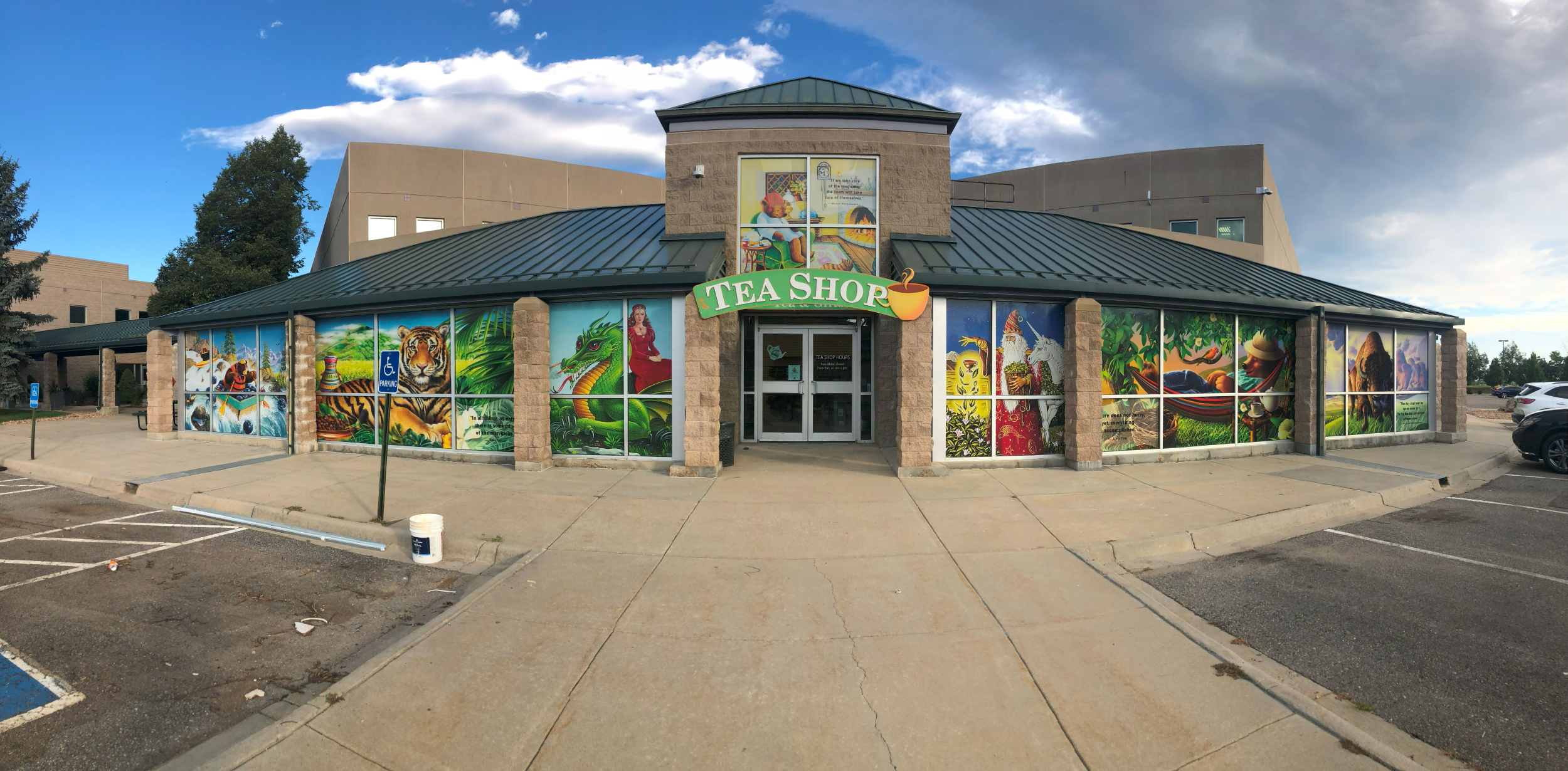 A panoramic view of the Celestial Seasonings storefront in Boulder, Colorado, featuring vibrant and detailed window wraps depicting various scenes including a tiger, a dragon, and other thematic elements related to tea and nature.