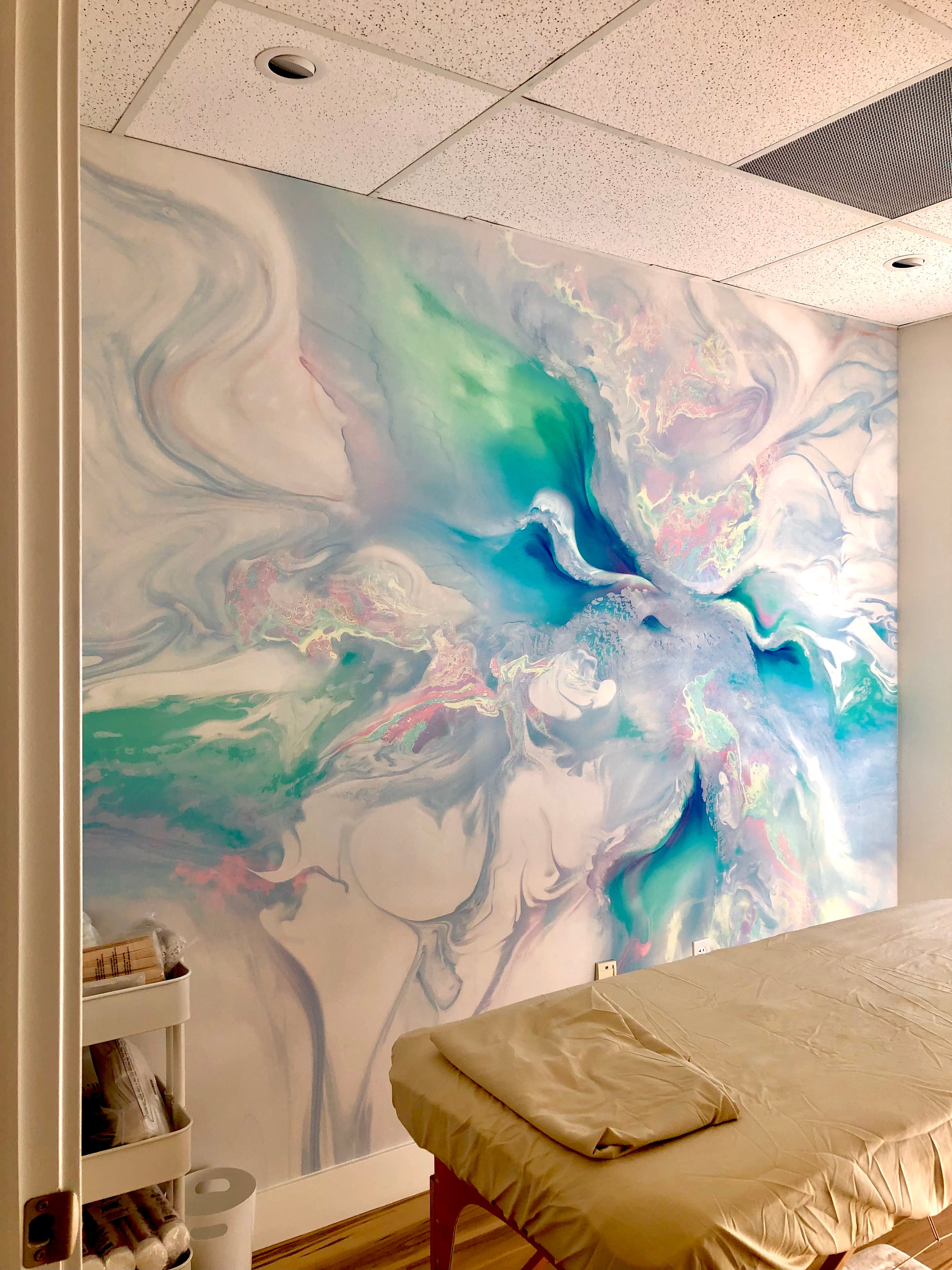 A soothing interior vinyl wall wrap located at The Body Bar in Lafayette, Colorado. The design features marbled swirls in calming tones of turquoise, blue, and soft white, creating a tranquil atmosphere in the massage room.