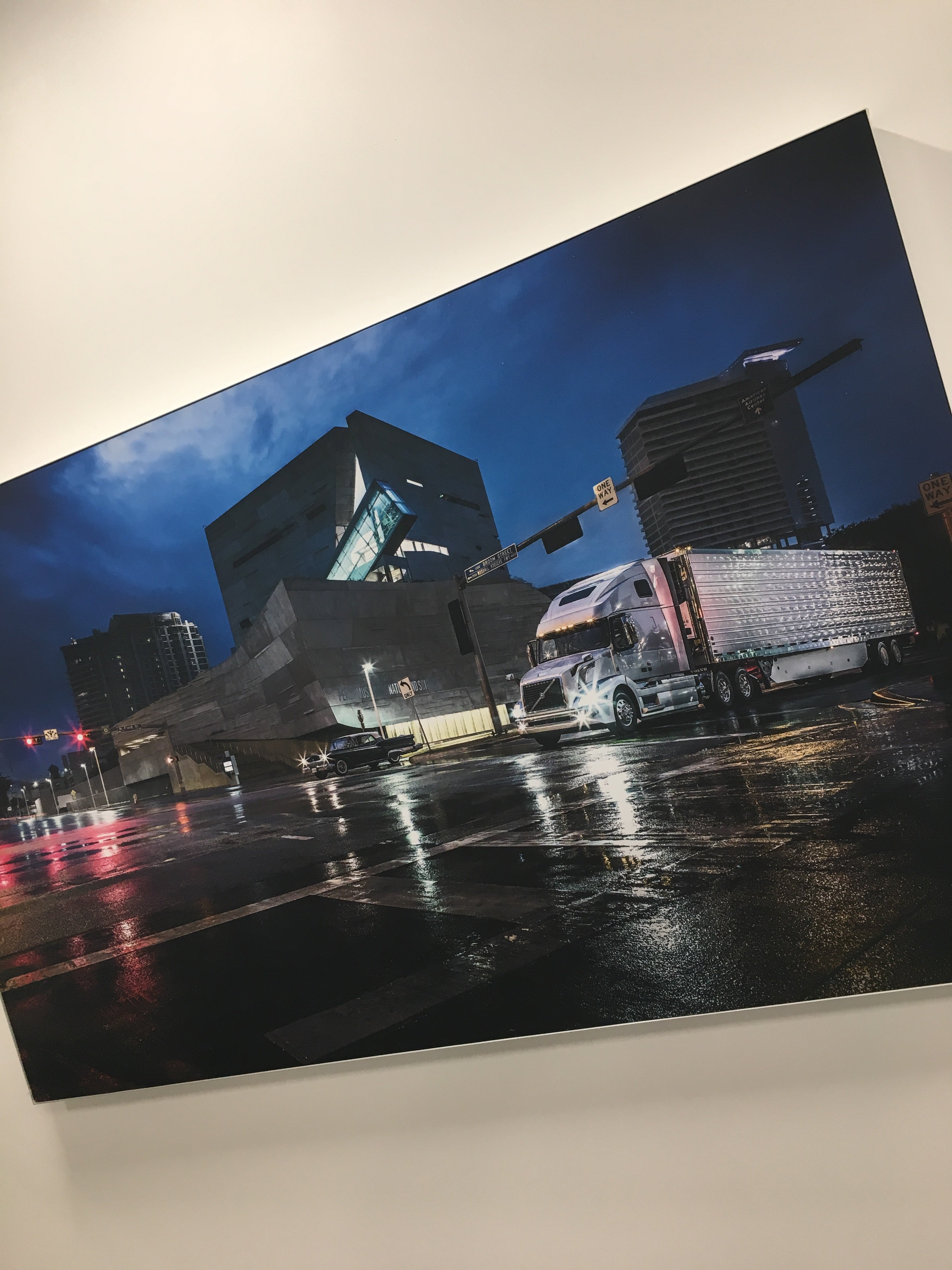 A Silicone Edge Graphic (SEG) Fabric Frame installed at Volvo Mack Headquarters in Atlanta, Georgia, featuring a night scene with a Volvo truck on a wet, reflective street in front of modern buildings.