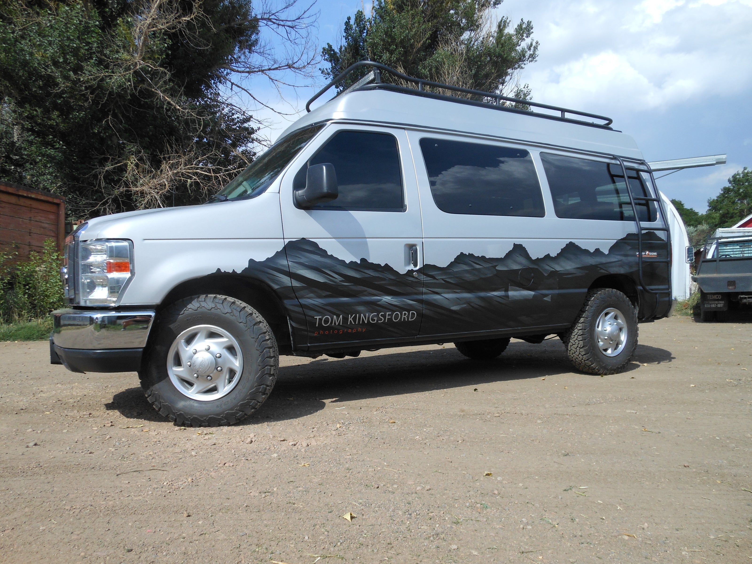 A partial vehicle wrap showcasing a rugged mountain range design for photographer Tom Kingsford's van, photographed from a side angle.