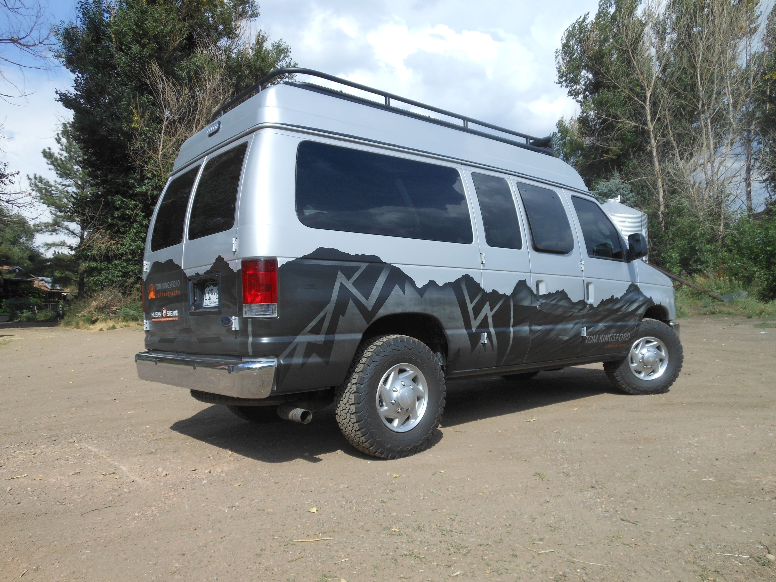 A customized van with a mountain-themed graphic wrap along the bottom half of the vehicle, designed for Tom Kingsford, a traveler and explorer. The design complements the outdoor nature of his brand.